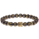 Om Mani Padme Hum black agate Buddhist bracelet with gold Sanskrit engraved beads and gold-plated Buddha head charm, studio flat lay view