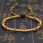 Om Mani Padme Hum Buddhist bracelet with bronze carved beads and beige stone accents on traditional calligraphy background