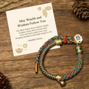 Om Mani Padme Hum Buddhist string bracelet with metal charm bell, multicolored woven cord, displayed with gift message card on wooden surface with natural pinecones