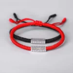 Couple of red and black Buddhist string bracelets with silver metal charms displayed on light gray background, adjustable drawstring closure design perfect for protection and good luck