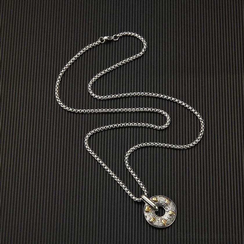 Om Mani Padme Hum Buddhist pendant necklace laid flat in top-down view with full box chain visible on solid black textured background, showing compact pendant size and chain length