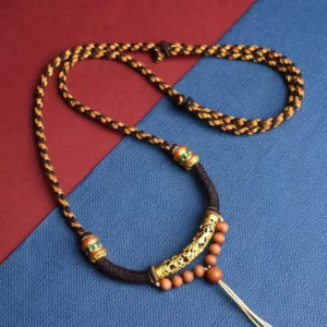 Om Mani Padme Hum Buddhist prayer necklace with King Kong knot pendant, carved gold bead and enamel details flat lay view