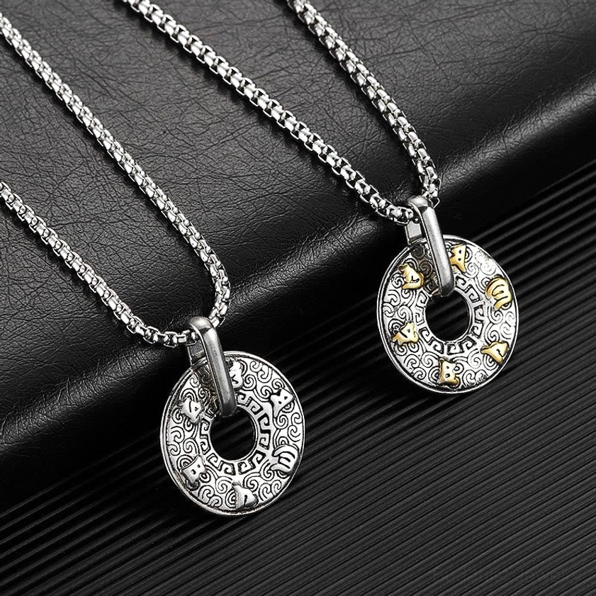 Pair of matching Om Mani Padme Hum Buddhist pendants on box chain necklaces displayed on black and striped leather background, showing identical spiritual pendant designs
