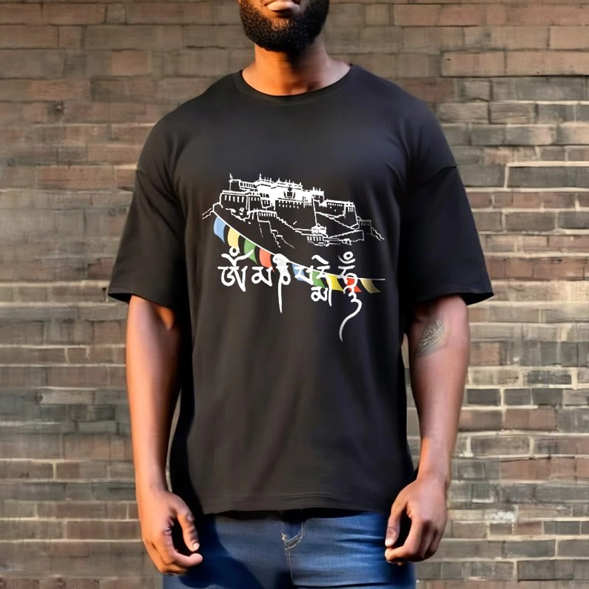 Male model wearing dark grey Buddhist prayer flag t-shirt with mantra design against brick wall background, styled with blue jeans