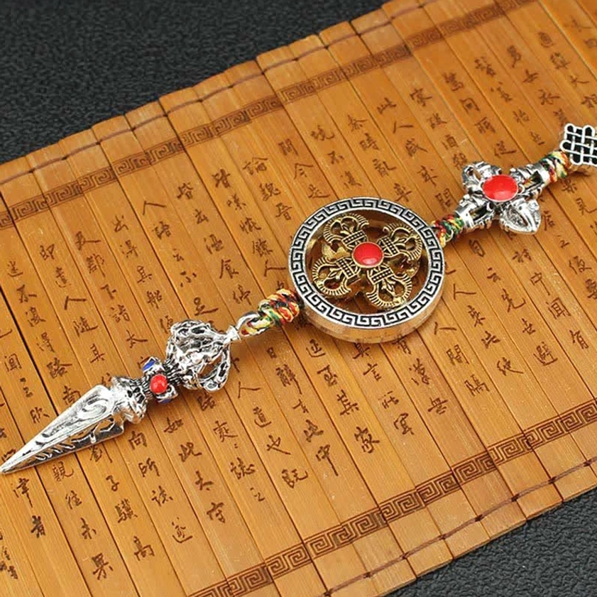 Overhead view of Buddhist car ornament with dharma wheel, braided rope, phurba and floral charms on calligraphy background