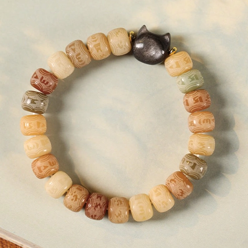 Close-up of Om Mani Padme Hum engraved bodhi beads on elastic bracelet with obsidian cat charm on neutral background