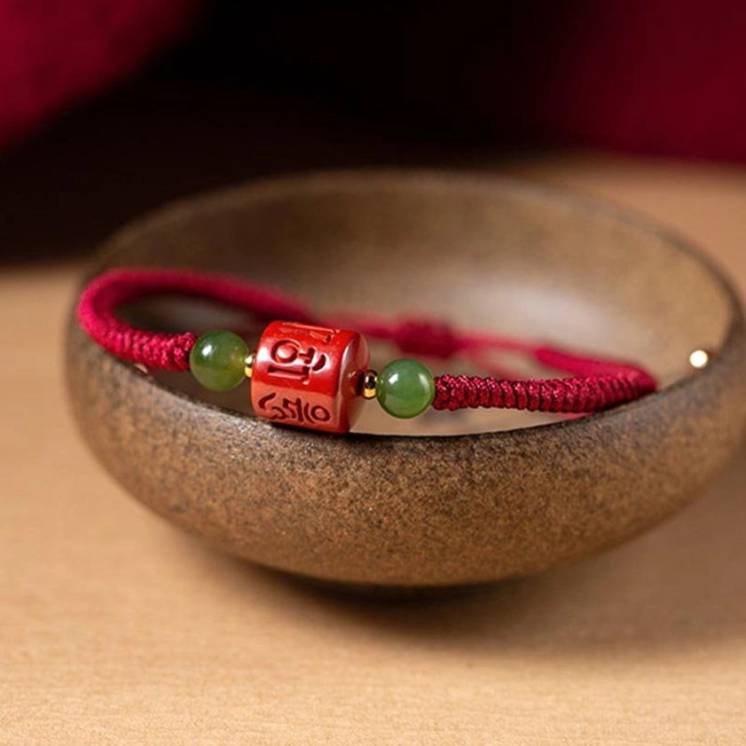 Om Mani Padme Hum cinnabar bracelet placed inside ceramic bowl, displaying full bead layout and rope weave