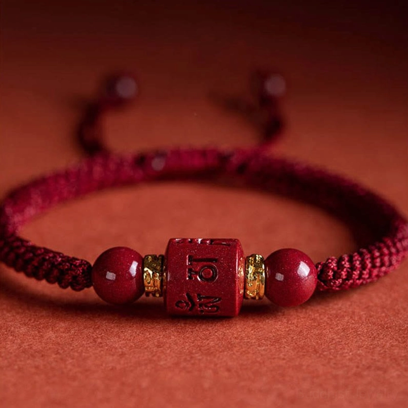 Close-up detail of red cinnabar Buddhist bracelet showing hand-engraved Sanskrit mantra, polished beads, and gold metal accents