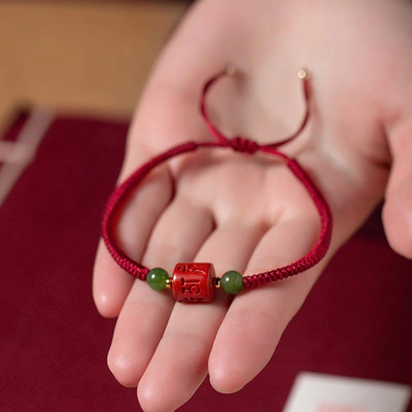Om Mani Padme Hum cinnabar bracelet in hand showing adjustable braided rope tail and complete bead set detail