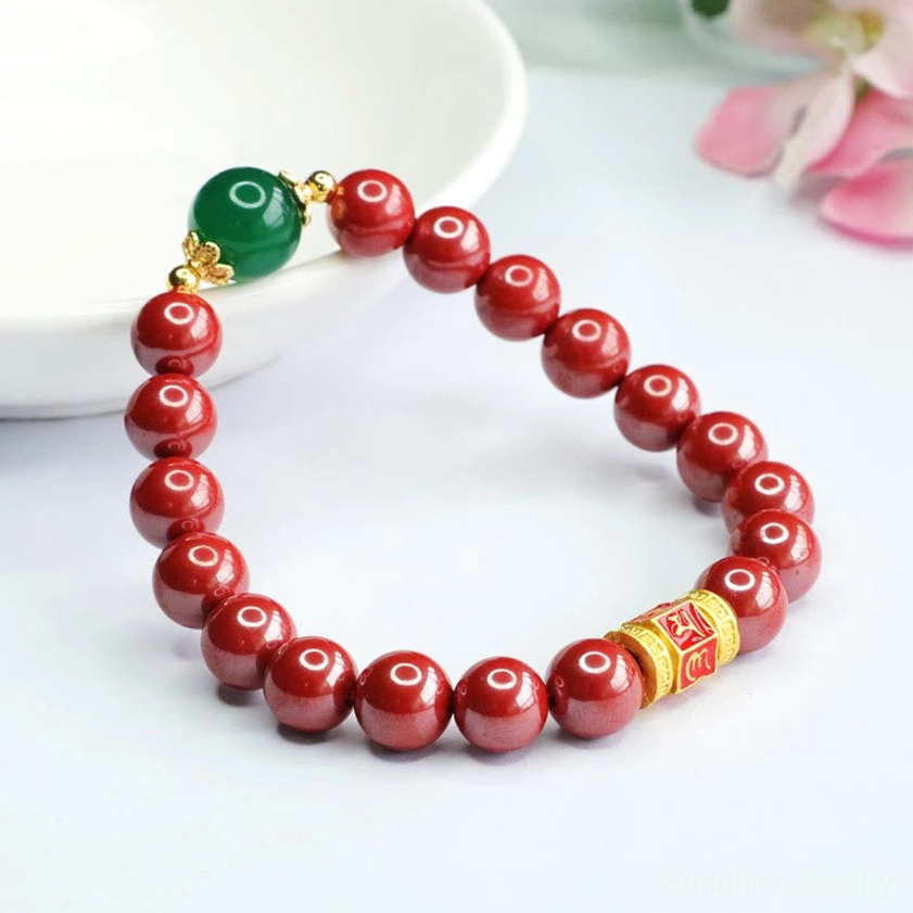 Buddhist mantra bracelet featuring natural cinnabar beads and green agate accent bead displayed on ceramic plate