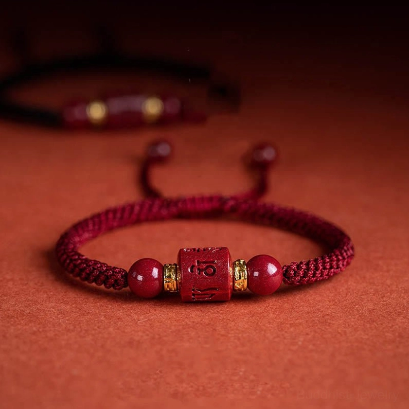 Om Mani Padme Hum cinnabar braided bracelet with red rope and engraved charm beads displayed on neutral background
