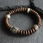 Brown coconut shell Om Mani Padme Hum bracelet with engraved silver mantra beads, flat lay view on dark slate