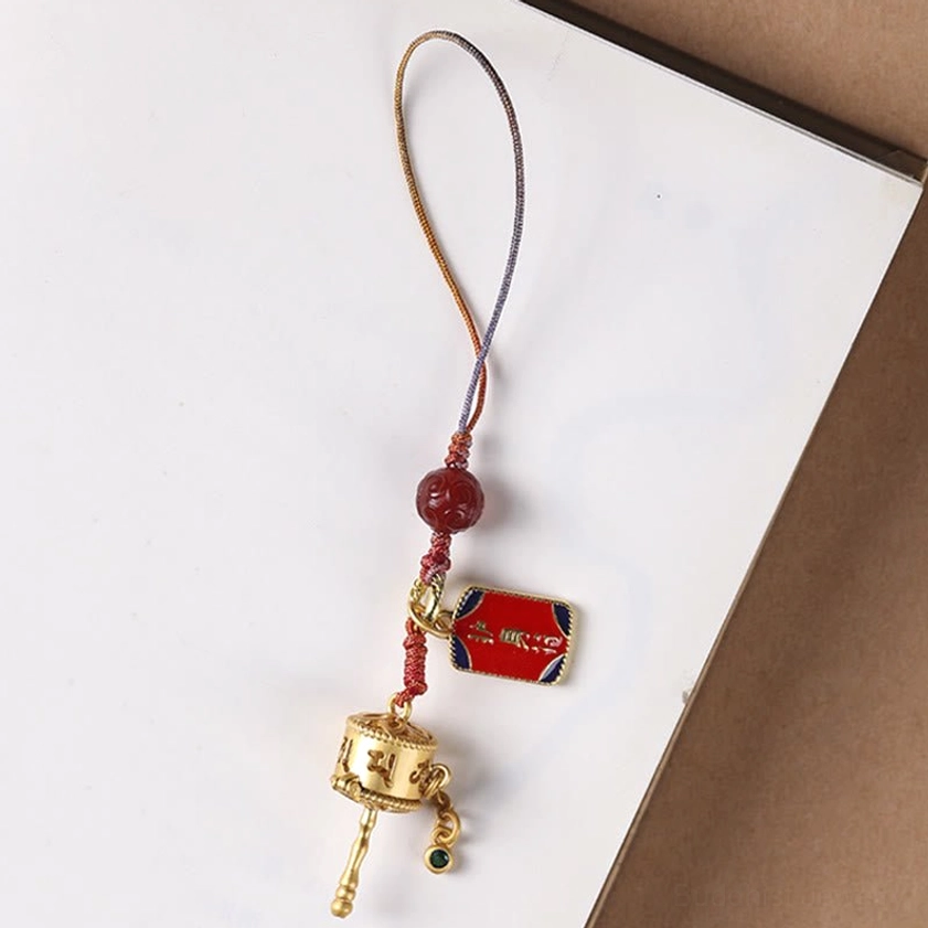 Single Om Mani Padme Hum prayer wheel charm with complete braided cord and red agate bead on notebook