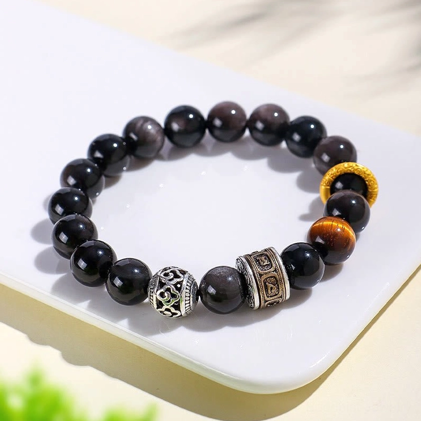 Close-up detail of embossed Om Mani Padme Hum copper barrel beads and obsidian stones in Buddhist protection bracelet