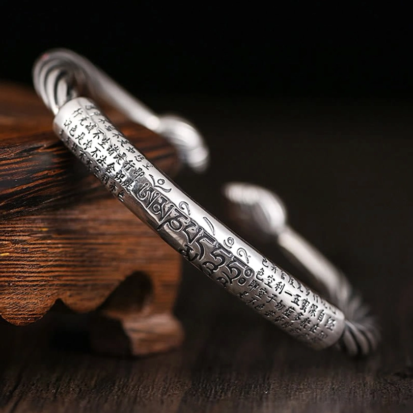 Om Mani Padme Hum copper cuff bracelet with hand-engraved sacred mantra text, twisted rope band design, vintage antique silver finish displayed on wooden table