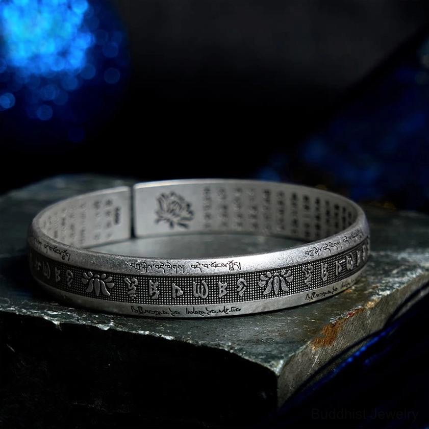 Buddhist mantra bangle showing inner lotus engraving and full sacred text, high-angle side view on stone with blue background