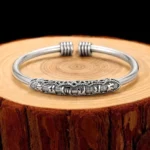 Om Mani Padme Hum engraved open cuff bracelet with oxidized silver finish and carved Sanskrit mantras displayed on wooden tree stump