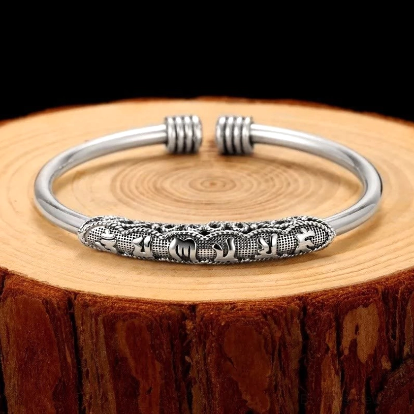 Om Mani Padme Hum engraved open cuff bracelet with oxidized silver finish and carved Sanskrit mantras displayed on wooden tree stump