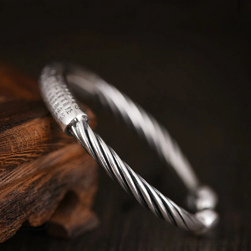 Oblique view of open-end sacred text cuff bracelet with partial mantra engraving on central bar, twisted full band design, and rounded end caps