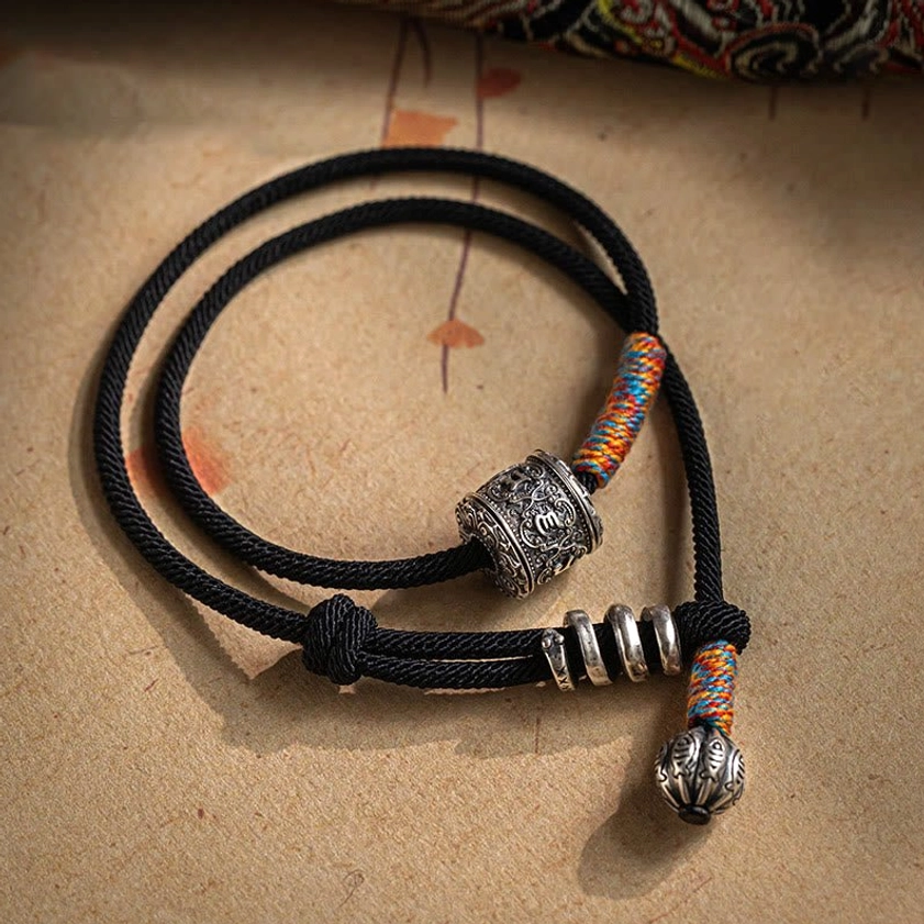 Om Mani Padme Hum double wrap bracelet with black braided cord, colorful woven trim, and silver beads on kraft paper background