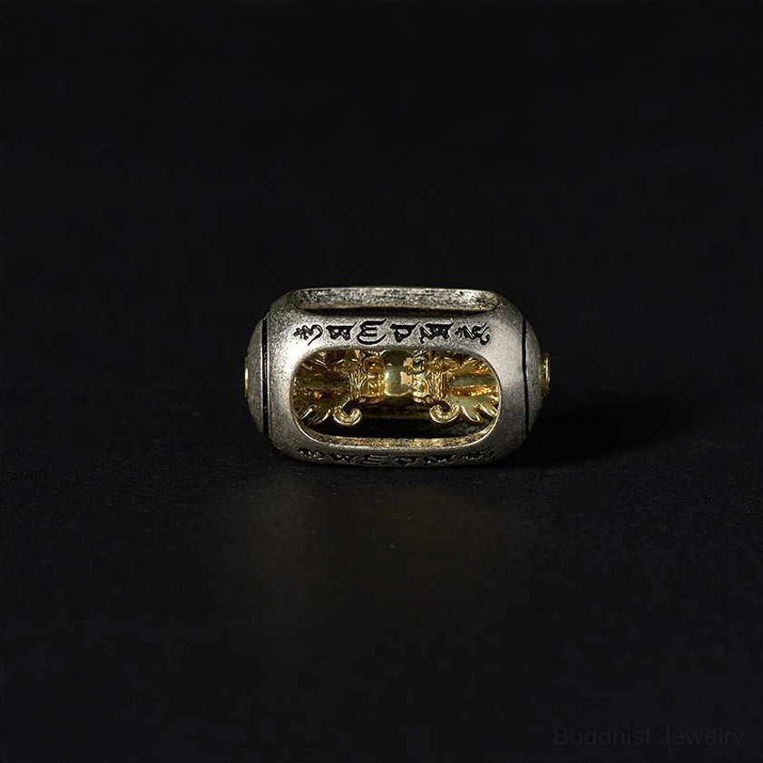 Close-up detail of single silver-toned metal charm bead with gold inlaid Om Mani Padme Hum mantra design on black background