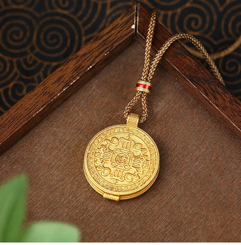Round gold amulet Buddhist pendant necklace displayed on wooden tray with green leaf accent, showing flat engraved mantra pattern on back