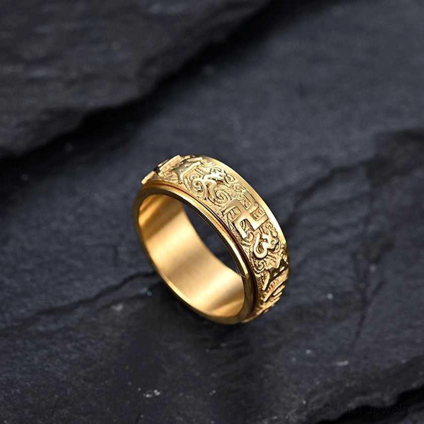 Gold-plated Six True Words titanium steel ring featuring embossed scroll and religious Sanskrit patterns, left side oblique view on dark background