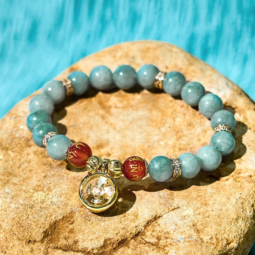 Detailed Om Mani Padme Hum jade mantra bracelet showing rotating gold pendant, red inscribed agate beads, and premium craftsmanship on natural stone surface