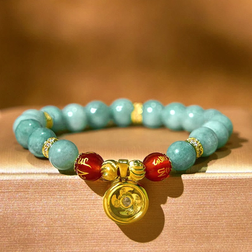 Handmade Buddhist mantra bracelet featuring natural jade beads, gold-plated spinning charm, and red carved sacred text beads displayed on brown fabric