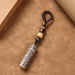 Om Mani Padme Hum copper keychain with Vajra pattern, top-down angle showing engraved pendant and Bodhi seed bead lanyard on wooden surface
