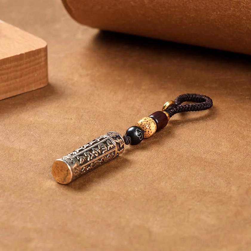 Flat lay front view of Om Mani Padme Hum keychain showing copper tube pendant with beaded woven lanyard and copper end cap detail