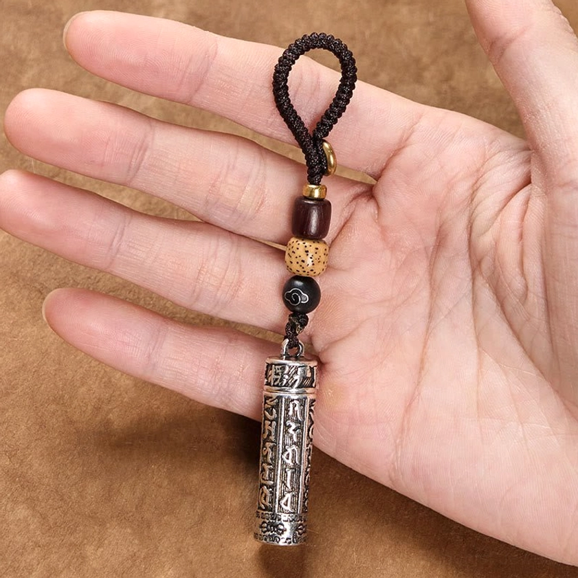 Hand holding Om Mani Padme Hum copper keychain with Vajra pattern showing engraved pendant and decorative Bodhi seed lanyard