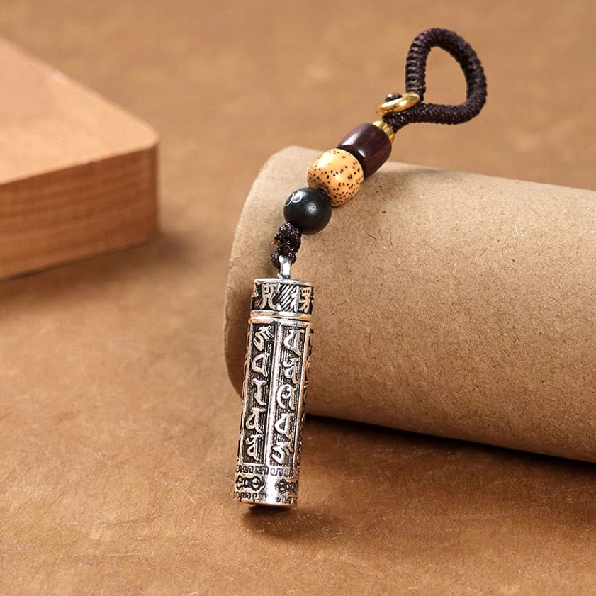 Left side angle view of Om Mani Padme Hum copper keychain with Vajra engraving and mixed bead woven lanyard on paper background