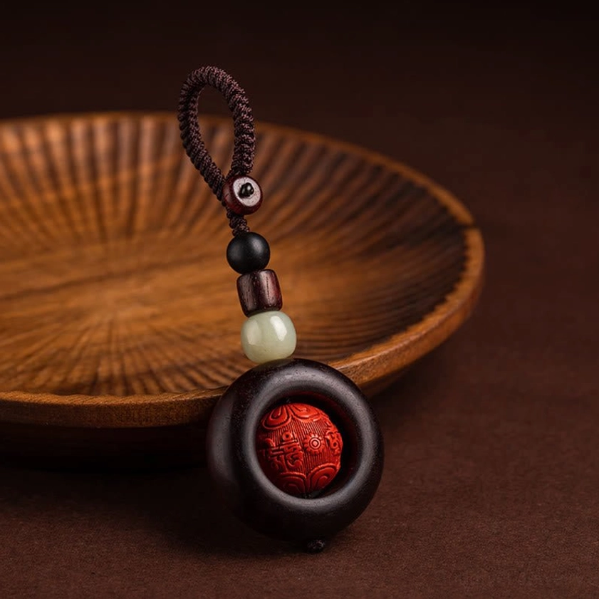 Single Buddhist keychain with Om Mani Padme Hum carved cinnabar bead and braided rope lanyard, side close-up view