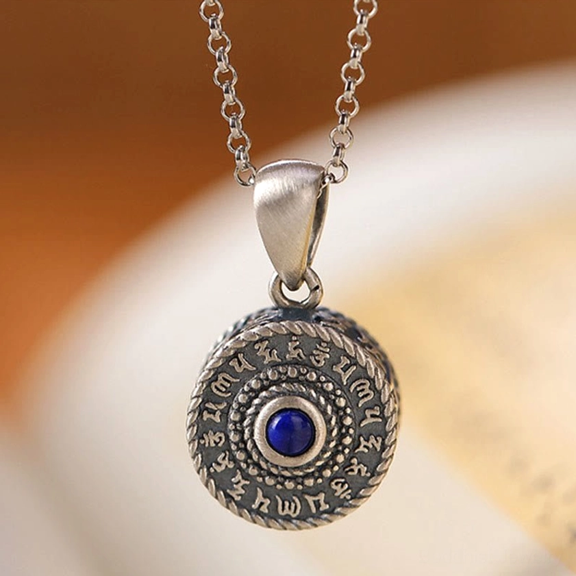 Close-up detail of 925 sterling silver Om Mani Buddhist pendant with deep blue lapis lazuli center stone and matte silver finish on neutral background