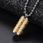 Om Mani Padme Hum prayer wheel pendant necklace in all golden titanium steel with hand-engraved lotus and Sanskrit characters, close-up oblique view on dark fabric background