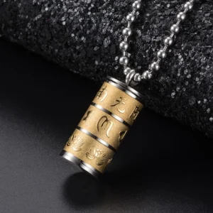 Om Mani Padme Hum prayer wheel pendant necklace in all golden titanium steel with hand-engraved lotus and Sanskrit characters, close-up oblique view on dark fabric background