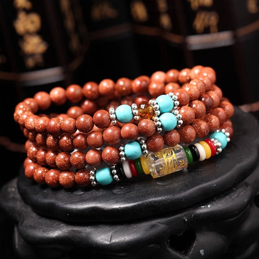 Close-up of Buddhist prayer beads mala with colorful spacers, turquoise dividers, and engraved mantra barrel bead on wooden display