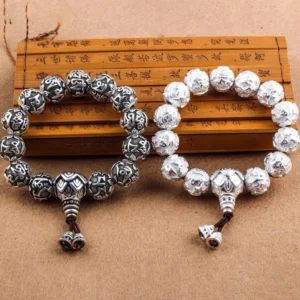 Om Mani Padme Hum carved silver alloy mala beads displayed on wooden Buddhist scripture, showing detailed mantra engravings and guru bead