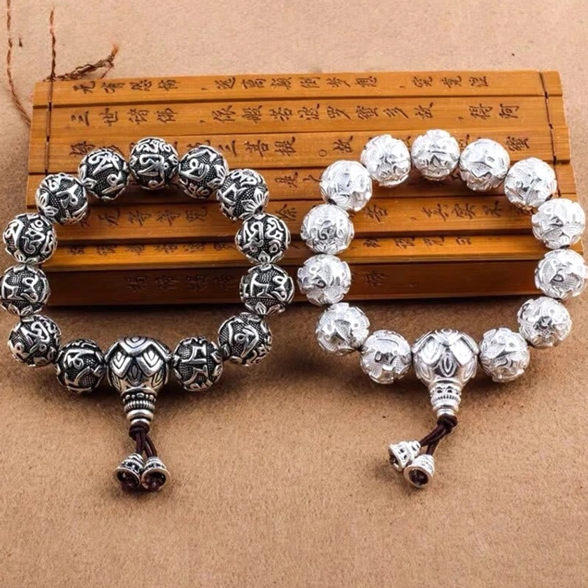 Om Mani Padme Hum carved silver alloy mala beads displayed on wooden Buddhist scripture, showing detailed mantra engravings and guru bead