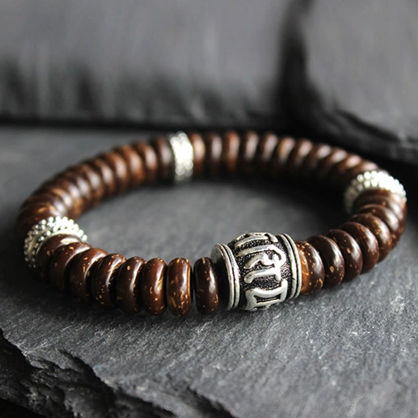 Close-up overhead view of Buddhist coconut shell bracelet showing central silver mantra barrel bead and brown disc beads