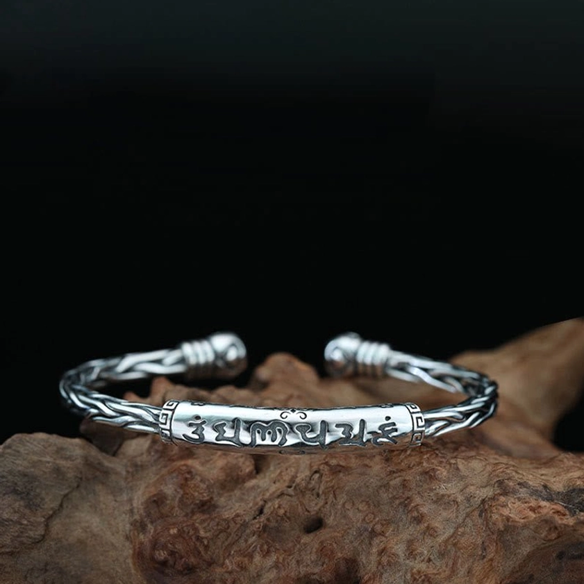 Sanskrit engraved Buddhist bracelet with braided chain body on wooden background
