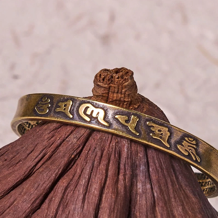 Antique bronze finish Om Mani Padme Hum cuff bracelet showing raised mantra motifs, worn on wrist side view