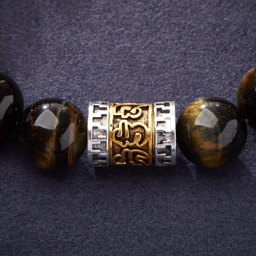 Close-up of Om Mani Padme Hum engraved metal charm accent with vintage gold-silver finish paired with striped tiger eye beads