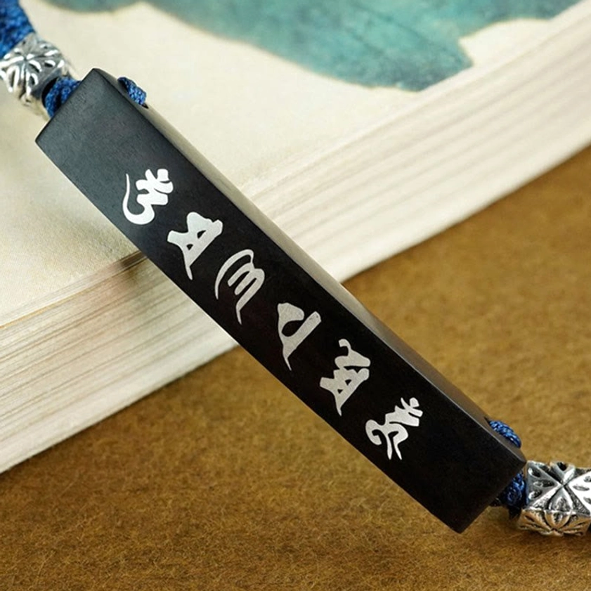Close-up detail of ebony plate featuring white Six True Words Om Mani Padme Hum mantra with silver carved connector, showcasing intricate wood-and-silver inlay craftsmanship