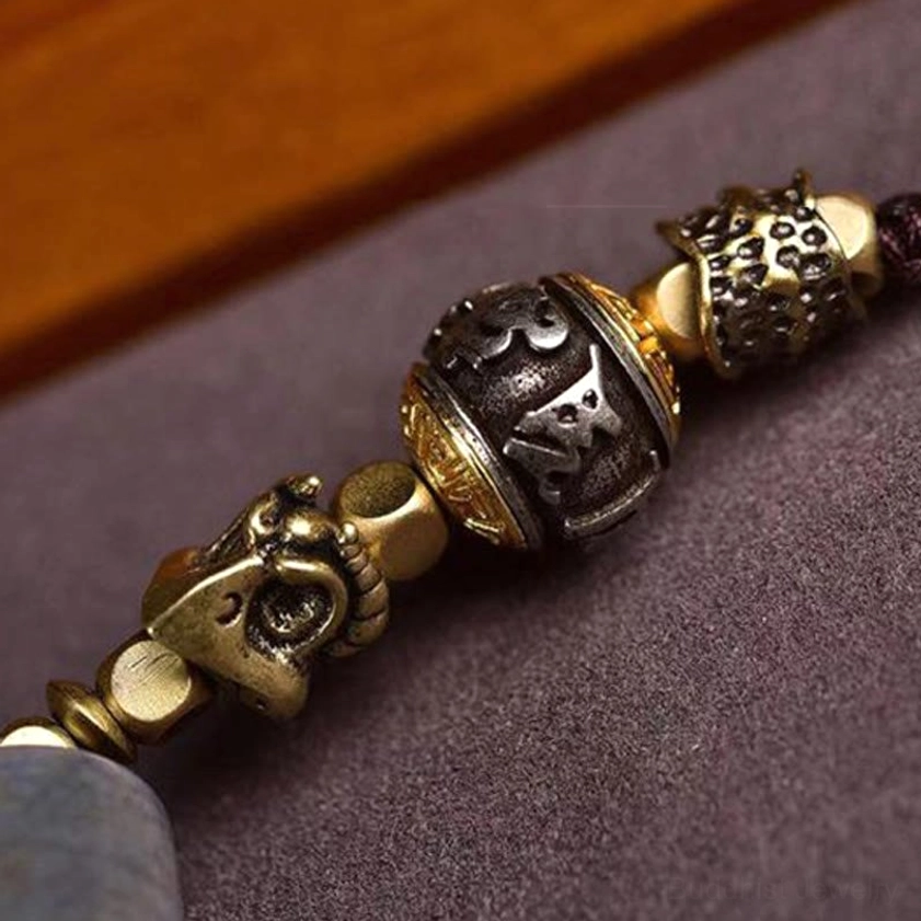 Extreme close-up of hand-carved metal mantra beads with engraved Om Mani Padme Hum text and aged two-tone bronze finish