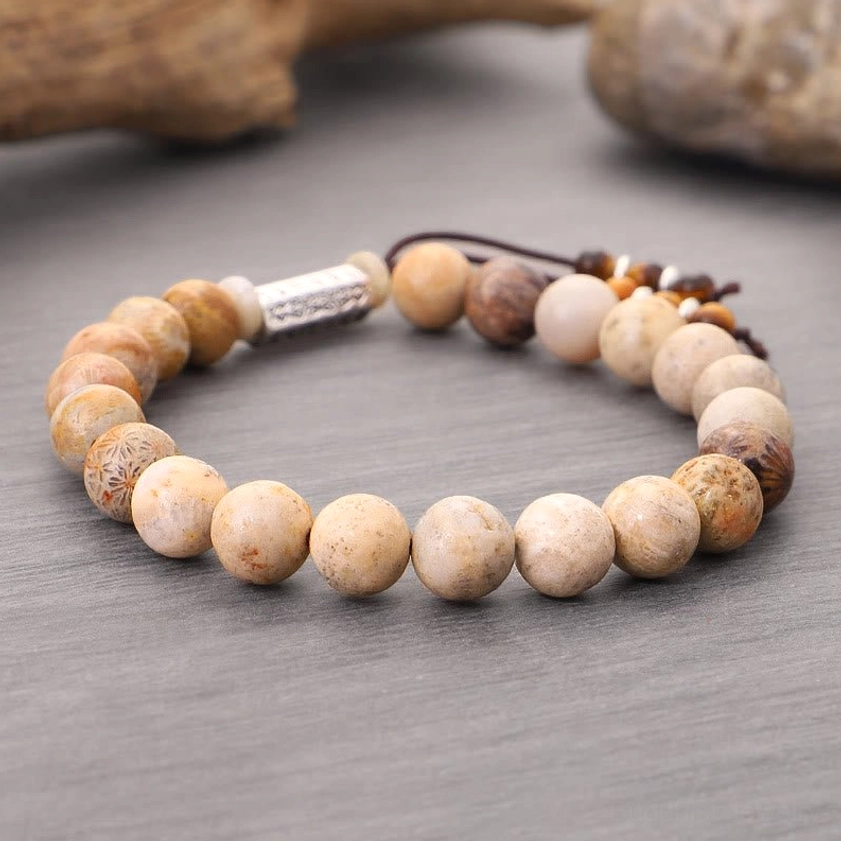 Side flat lay of weathered stone bracelet with varied warm-tone natural beads, metal mantra charm, and detailed tassel