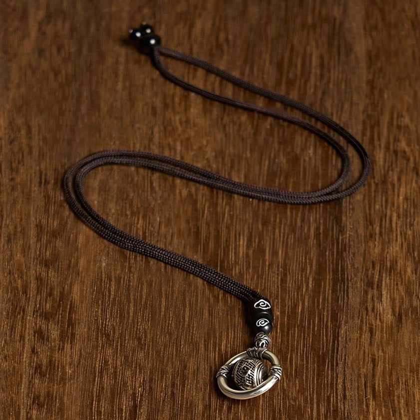 Buddhist necklace with braided cord featuring silver engraved Om Mani Padme Hum pendant and black accent beads, flat lay