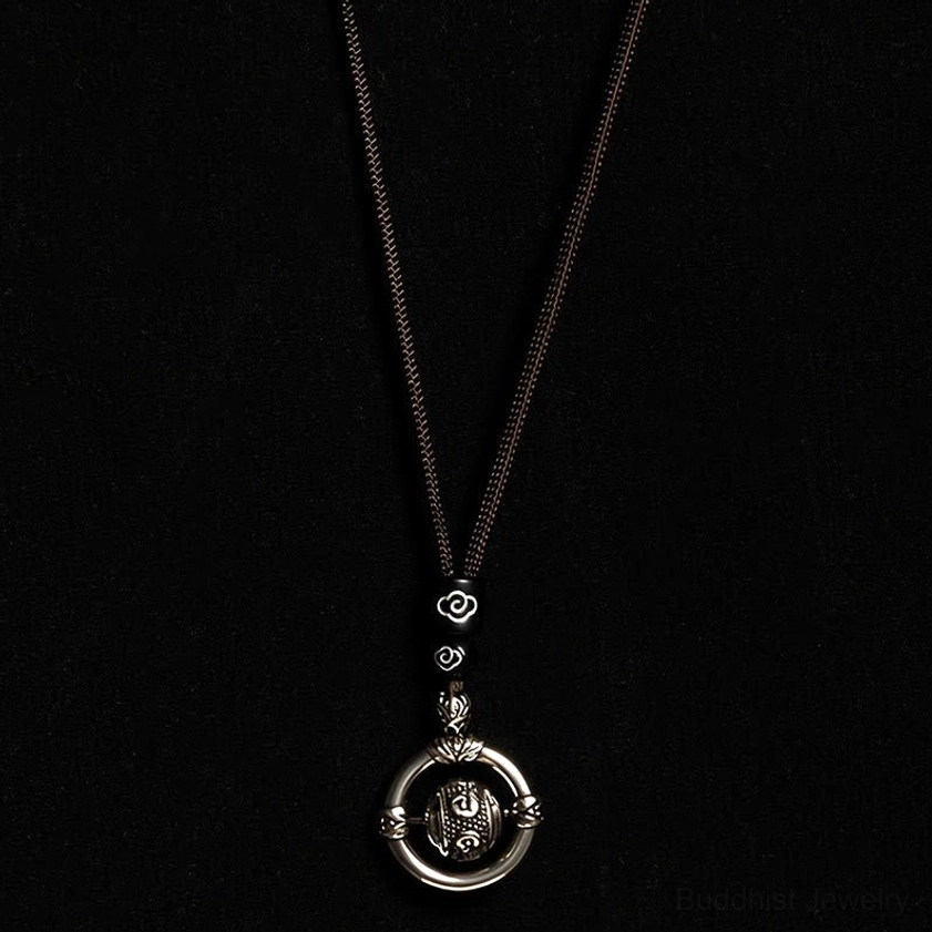 Full vertical view of Om Mani Padme Hum Buddhist necklace with brown braided rope and vintage silver rotating pendant on dark background