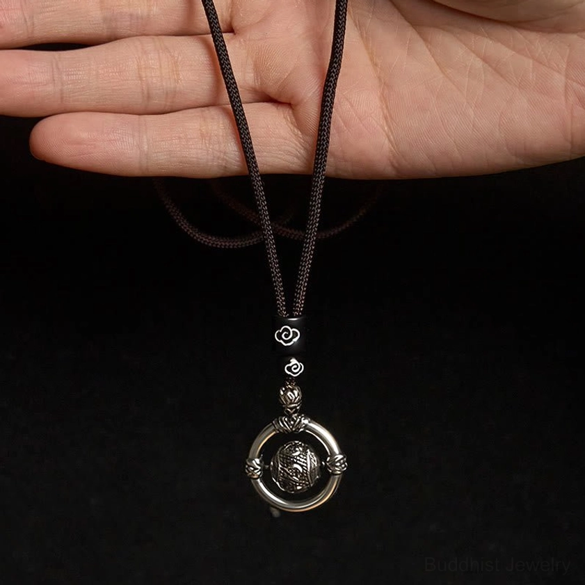 Om Mani Padme Hum necklace worn on hand showing black braided rope with vintage silver rotating pendant, eye-level close-up